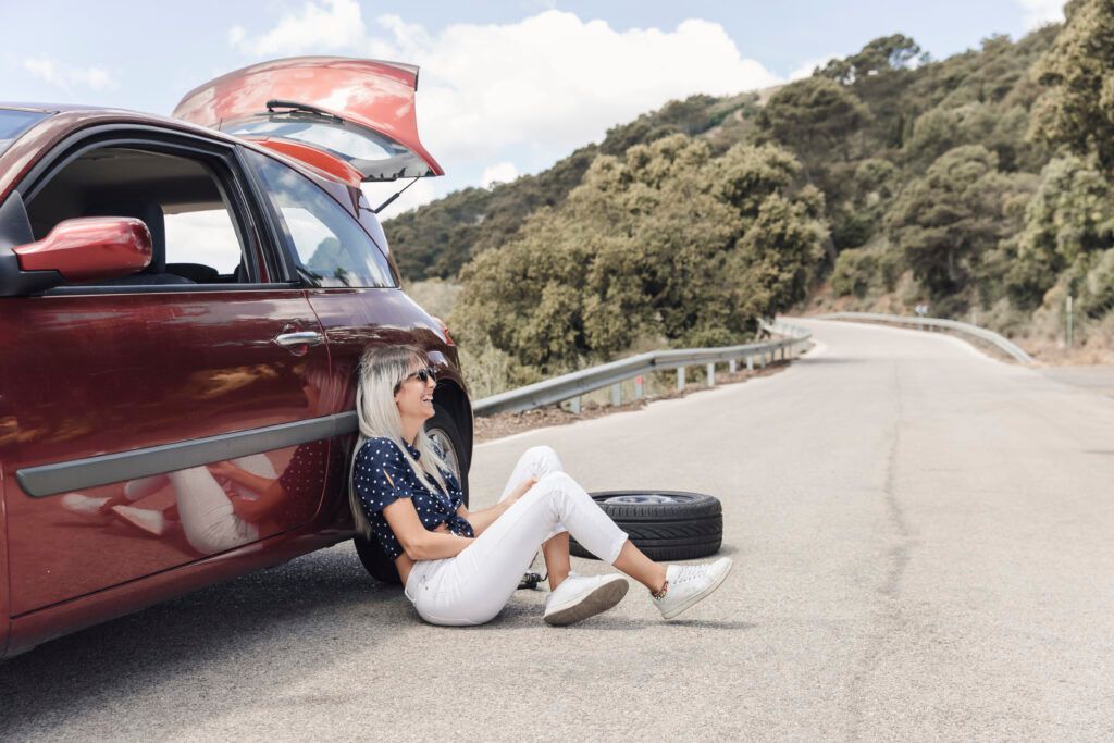 happy-woman-sitting-near-broken-down-car-winding-road-1024x683.jpg