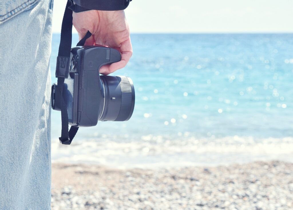 cropped-hand-man-holding-camera-beach-against-sky-1024x733.jpg